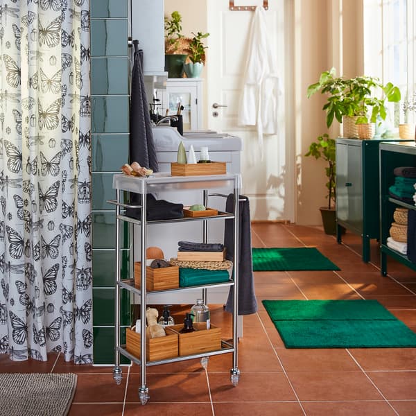 A GRUNDTAL trolley in stainless steel is standing next to a shower, and the shelves have shower products on them.
