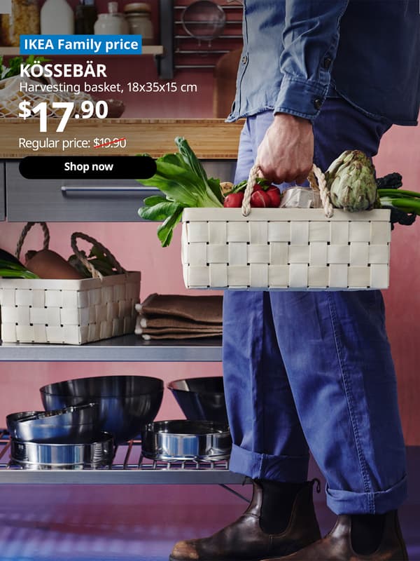 A guy in blue outfit is carrying a KÖSSEBÄR harvesting basket filled with fresh vegetables in a kitchen setting with a RIMFORSA work bench next to him. Blue tag with white text that reads "IKEA Family price". Followed by white text over image that reads "KÖSSEBÄR , Harvesting basket, 18x35x15 cm, Price $17.90" Regular price: $19.90 with red line slashed across.