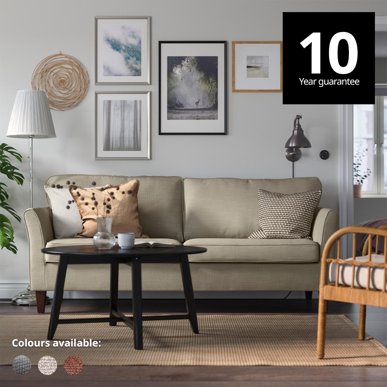 A hakebo beige EKHOLMA 3-seater sofa in a living room setting. A 10-year guarantee tag is placed over the image at the top right corner. White text overlay image that reads "Colours available:" with the colour swatch of Hallarp beige, Hallarp grey and Saxemara black-blue.