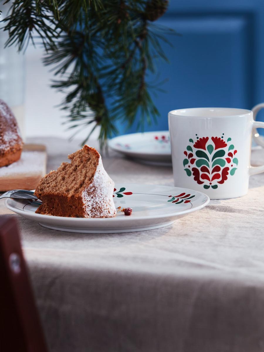 A half-eaten slice of cake is placed on a VINTERFINT plate. The VINTERFINT mug with scandinavian floral pattern is placed nearby the plate.