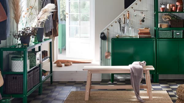 A hallway containing a NORRÅKER bench and KOLBJÖRN shelving units and cabinets holding boxes, household objects and plants.