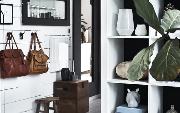 A hallway decorated with hooks and handbags, mirrors and a white shelving unit displaying everyday objects.