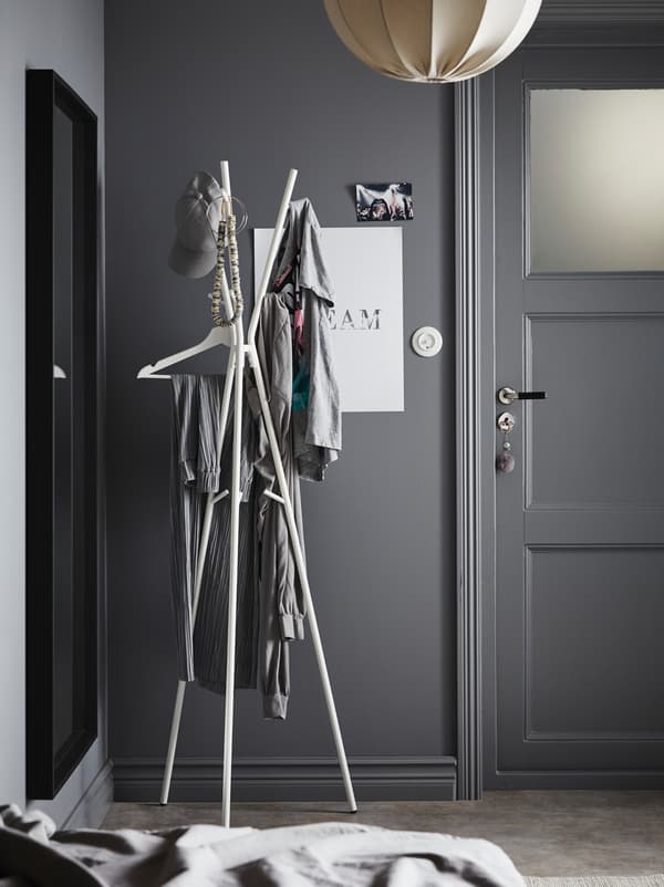 A hallway painted completely in gray with a white lamp and a white, minimalistic EKRAR hat and coat stand with three legs.