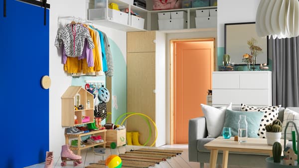 A hallway that opens into a living room. There is a PLATSA wardrobe on one side, with open shelving units above it.