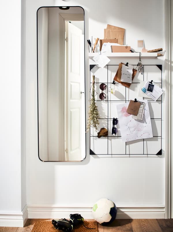 A hallway wall with a full length mirror, a small shelf and a black SÖSDALA memo board in steel.
