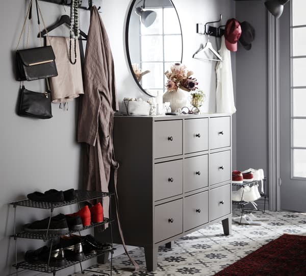A hallway with a symmetric storage combination made from a grey BRYGGJA chest of nine drawers, hooks, and shoe racks.