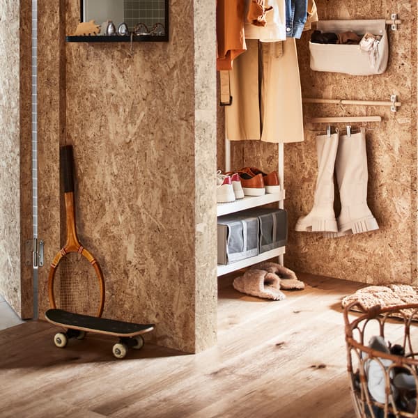 A hallway with a white coat rack with shoe storage, a rattan basket with shoes plus a rail with boots on a skirt hanger.