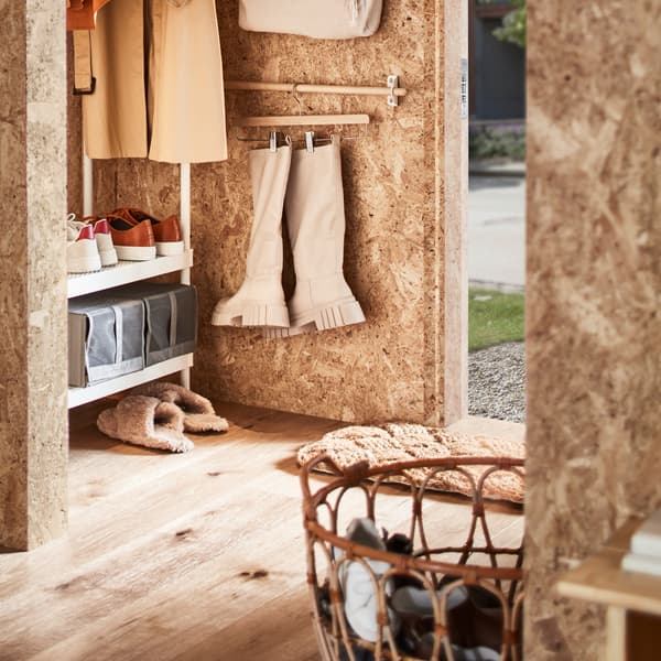 A hallway with a white coat rack with shoe storage, a rattan basket with shoes plus a rail with boots on a skirt hanger.