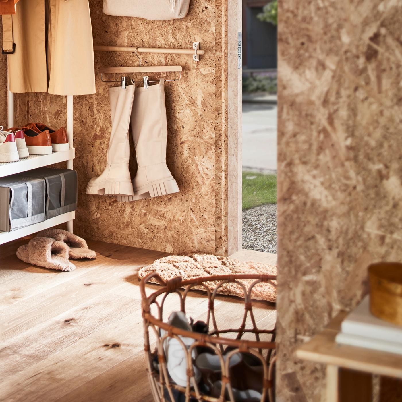 A hallway with a white coat rack with shoe storage, a rattan basket with shoes plus a rail with boots on a skirt hanger.