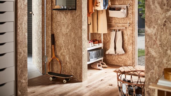 A hallway with a white coat rack with shoe storage, a rattan basket with shoes and wall rails with boots on a skirt hanger.