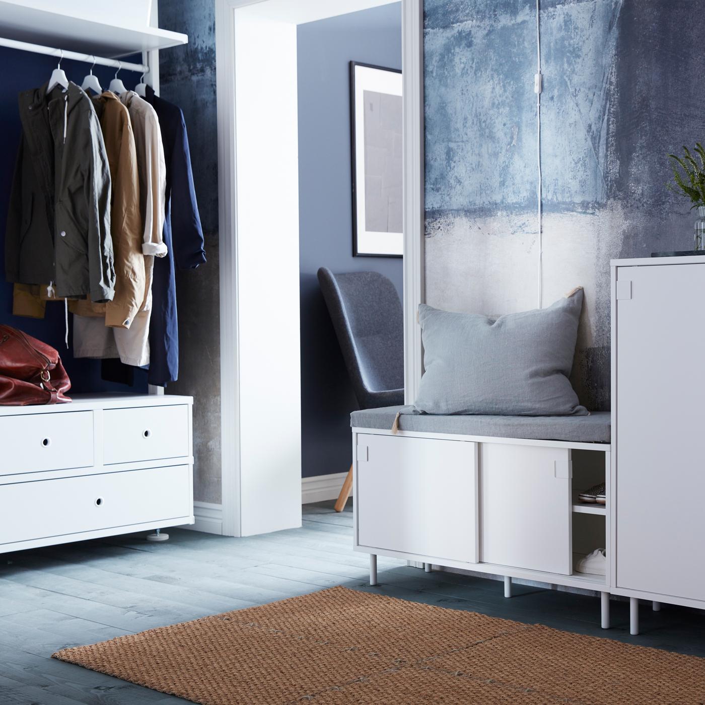 A hallway with a white MACKAPÄR cabinet and bench, a white chest of drawers, and four coir door mats together on the floor.