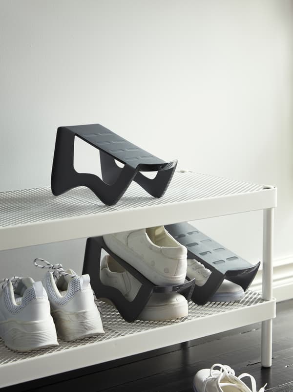 A hallway with a white shoe rack with two mesh shelves.
