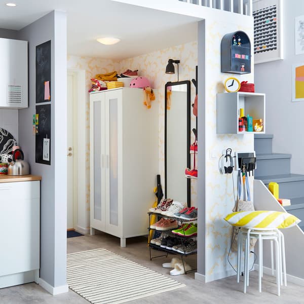 A hallway with ANEBODA wardrobe, a GREJIG shoe rack, a mirror and a white carpet on the floor and stairs in the background.