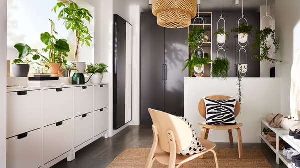 A hallway with dark grey PAX wardrobes, SINNERLIG bamboo lamp, and STÄLL shoe cabinets underneath a windowsill with plants.