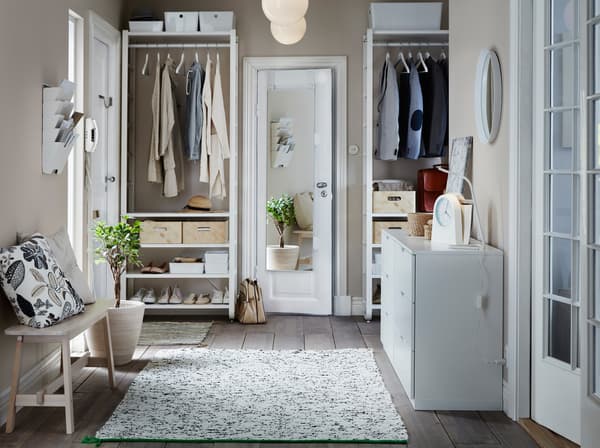 A hallway with floor-to-ceiling storage, with white IKEA ELVARLI shelves and clothes rails for hanging clothes and shoes.