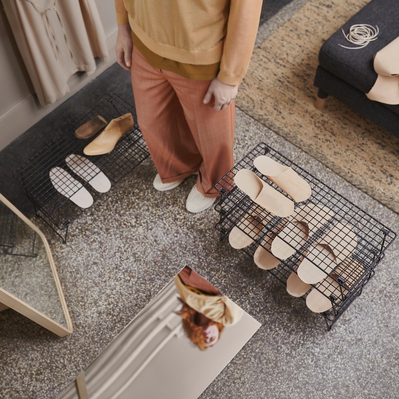A hallway with grey GREJIG shoe racks holding slippers, a person standing between them, plus two mirrors on the floor.