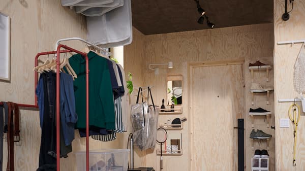 A hallway with shelving, hooks and a red NIKKEBY clothes rack and a white MULIG clothes bar both holding clothing.