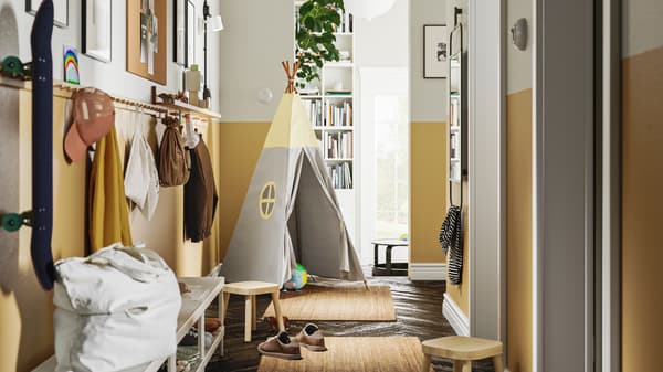 A hallway with two LOHALS rugs on the floor, and a line of HÖVOLM racks with 6 knobs along the wall holding bags and hats.