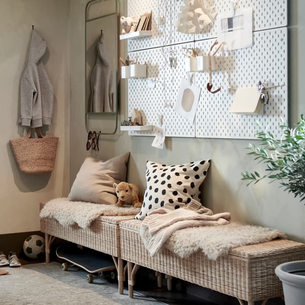 A hallway with two rattan benches with storage, a wall with white pegboards and a green mirror, plus a large potted plant.
