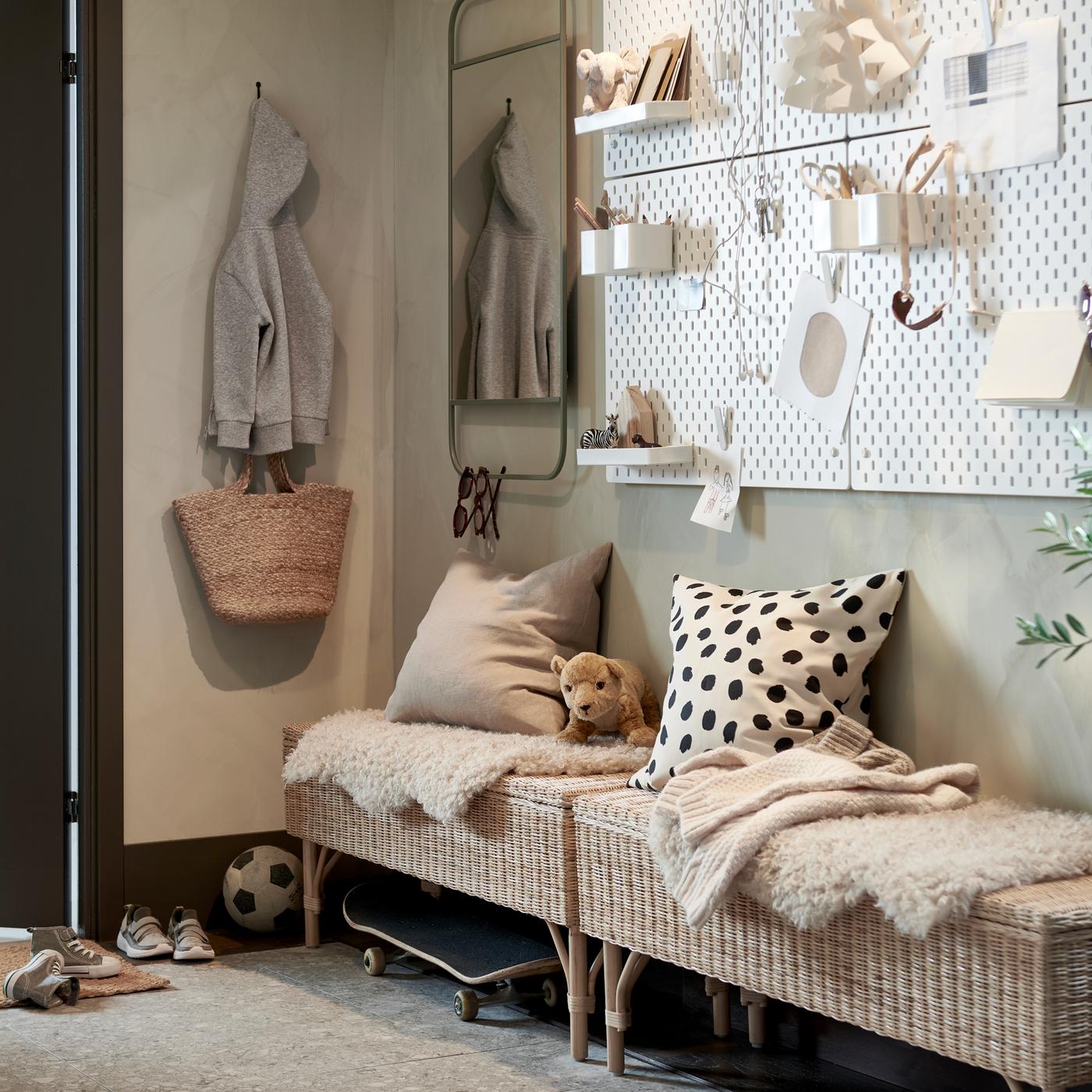 A hallway with two rattan benches with storage, a wall with white pegboards and a green mirror, plus a large potted plant.