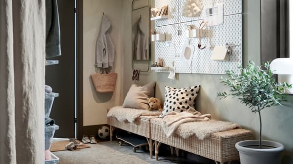 A hallway with two rattan benches with storage inside and cushions and rugs on top, plus white pegboards and a green mirror.