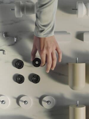 A hand grabs a black part. On a table, various loose parts of a piece of furniture are spread out.