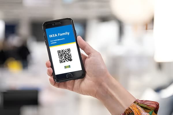 A hand holding a phone displaying the text “IKEA Family” and a QR code on the screen.