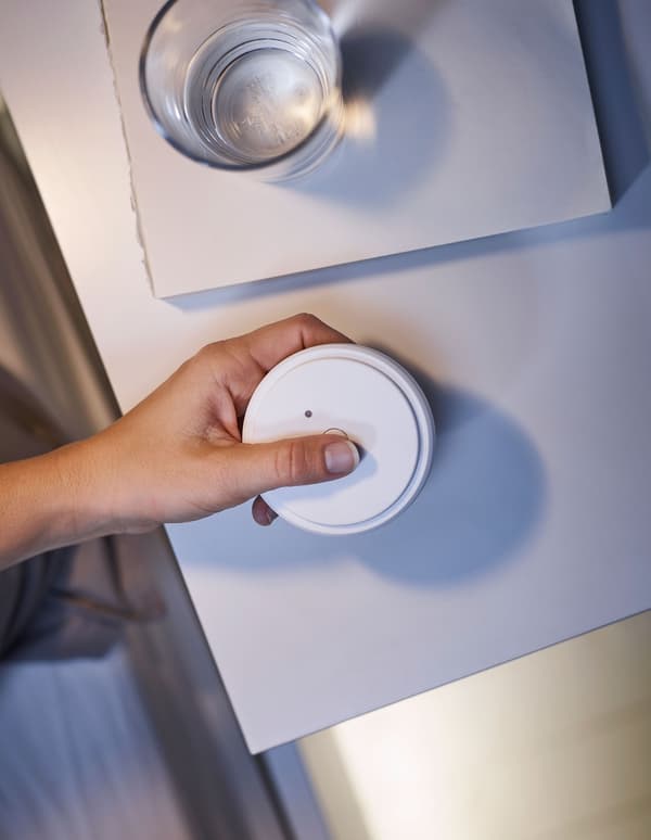 A hand holding a remote control, to adjust the lighting underneath a bedframe.