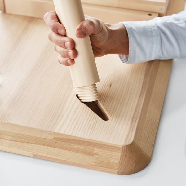 A hand holding a table leg and assemblying it to an IKEA tabletop