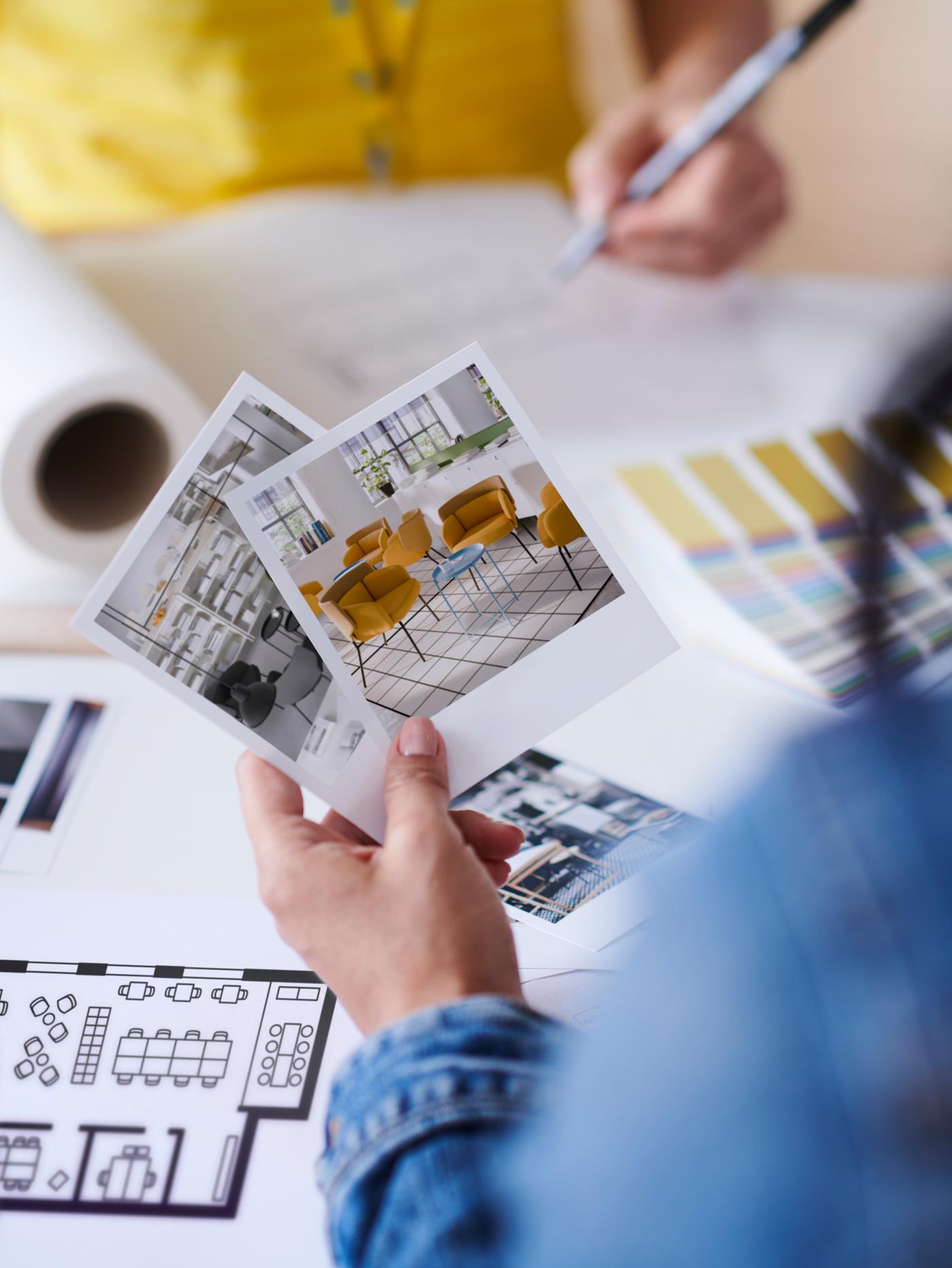 A hand holding photos of chairs and other items, while an IKEA co-worker in yellow top makes notes in the background.