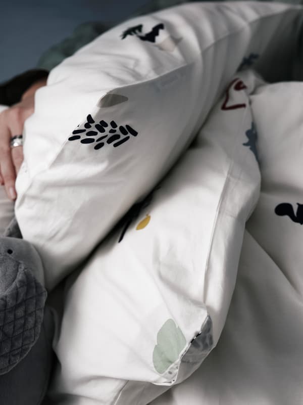 A hand is loosely draped over a BARNDRÖM duvet cover and pillowcase that has a forest animal pattern.
