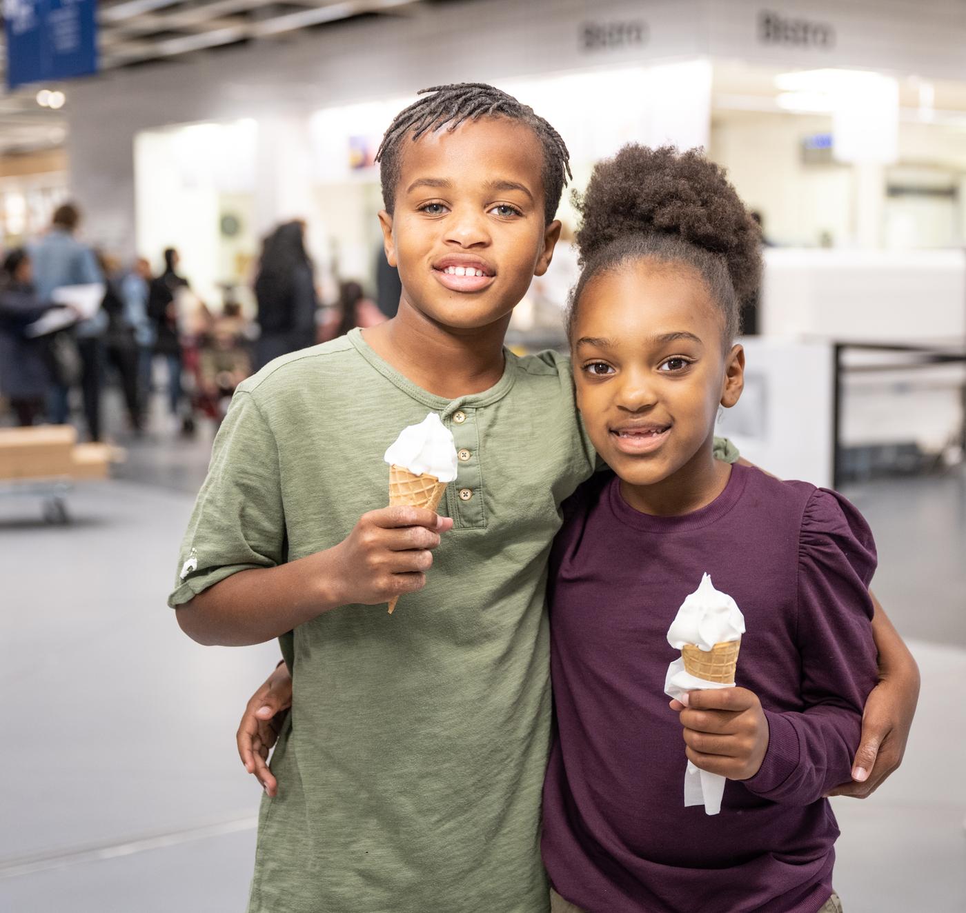A hand of a person wearing a grey top and purple nail varnish holding an ice-cream cone filled with strawberry soft ice.