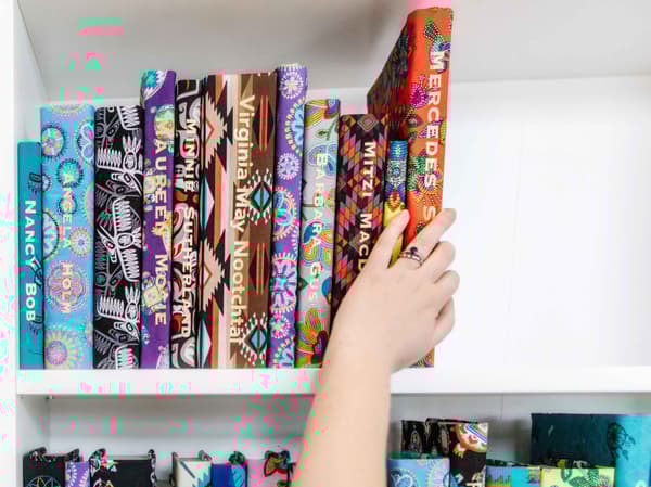 A hand placing books wrapped in fabric with names printed in gold on each book spine onto a bookcase.