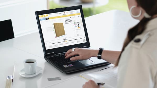 A hand pointing to a tablet screen showing a kitchen with base cabinets, high cabinets, worktops, a hob and an oven.