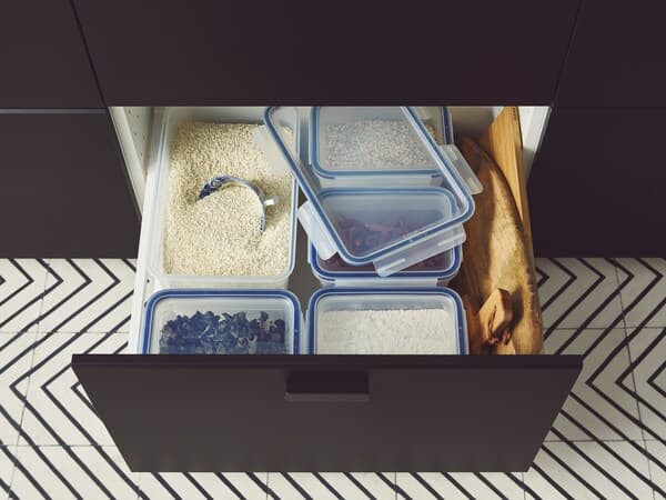A hand pulling out a drawer below a dark wood countertop with wooden inserts filled with kitchen utensils.