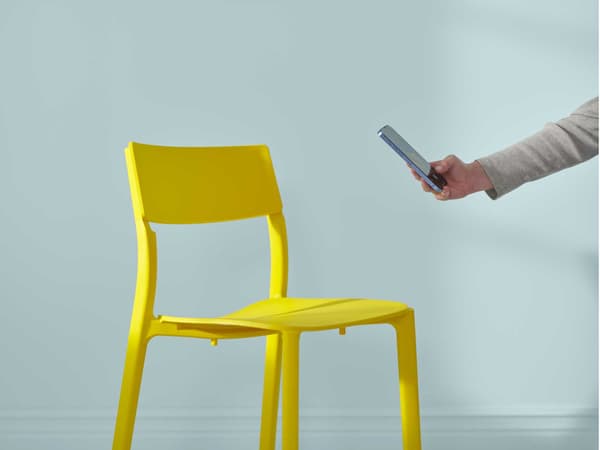 A hand reaches out to take a phone picture of a yellow IKEA chair.