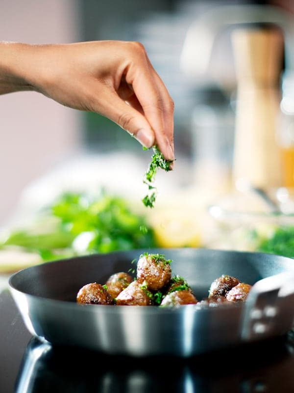 A hand seasoning HUVUDROLL plant balls in a IKEA 365+ frying pan.