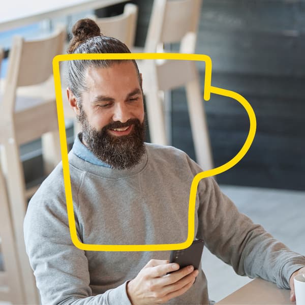 A happy man drinking coffee and checking his mobile phone.