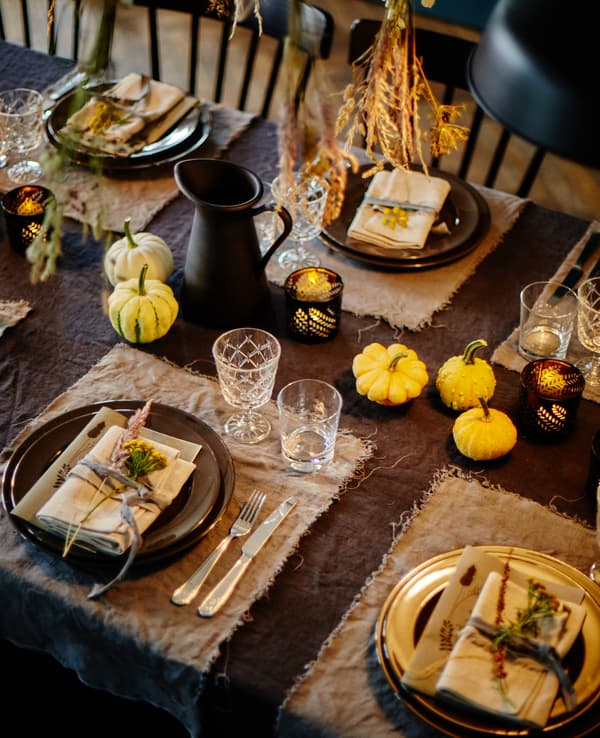 A harvest-themed dinner table setting in natural tones with dyed linens and small, decorative pumpkins.