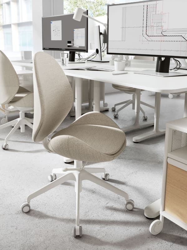 A HATTEFJÄLL office chair with beige fabric cover positioned in front of a white desk that has a computer on it.