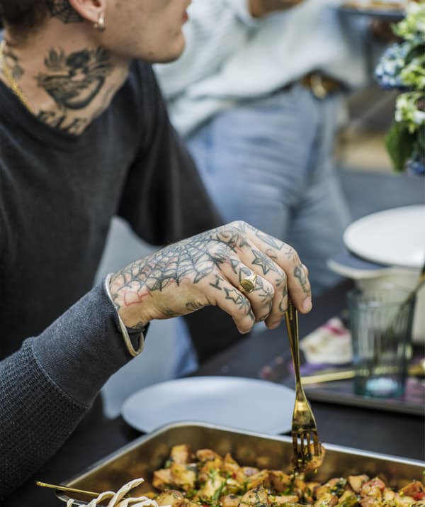 A heavily tattooed man holding a fork above a tray of food.