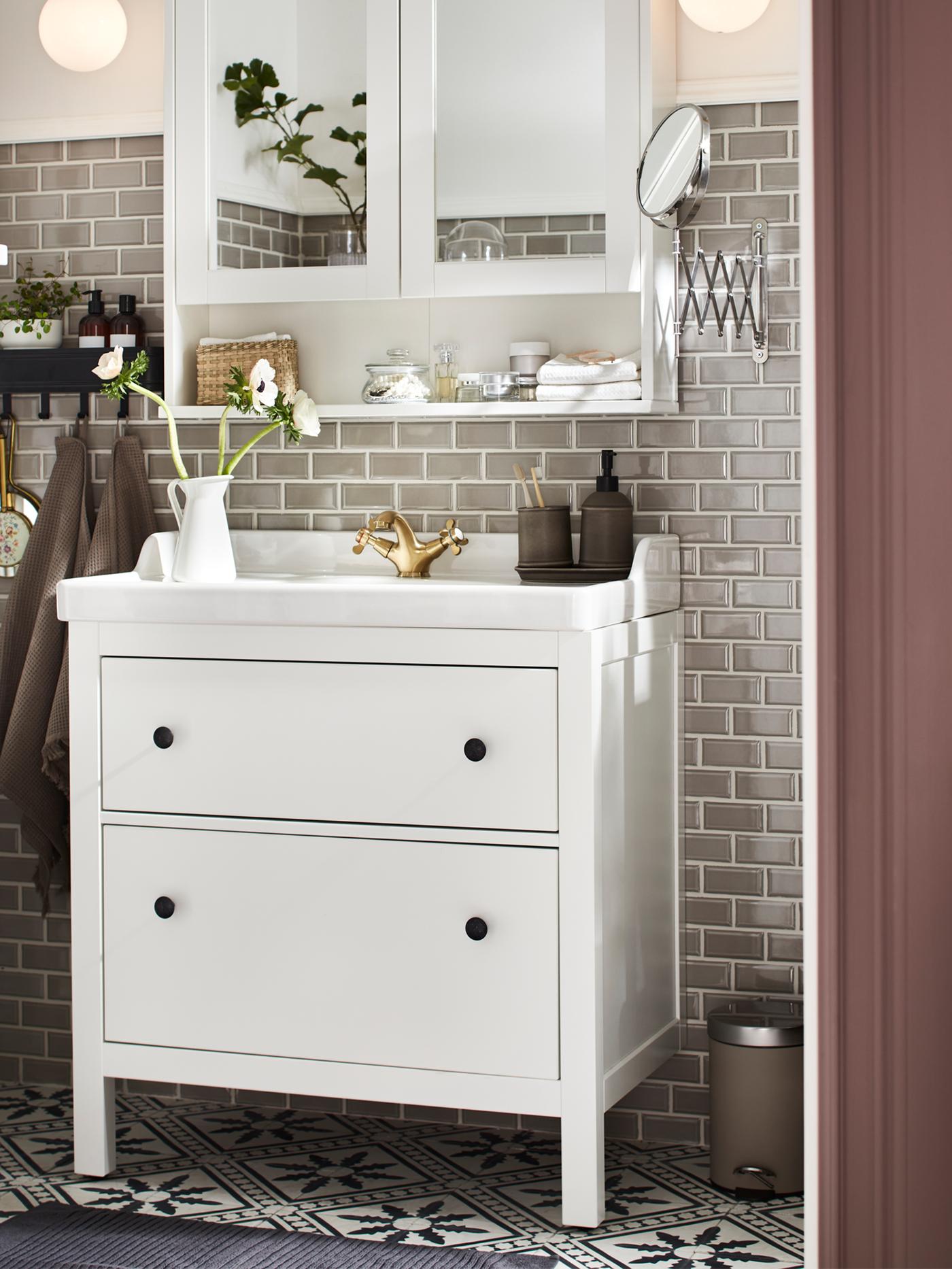 A HEMNES mirror cabinet in white with bathroom items on the shelf and a HEMNES/RÄTTVIKEN washstand with two drawers in white.