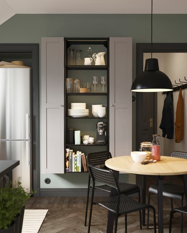 A high shelving unit in anthracite, two high cabinets in grey, a round wooden table, black chairs and a black pendant lamp.