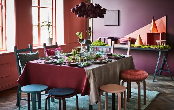 A holiday table is set using dark reds and greens, and greenery.