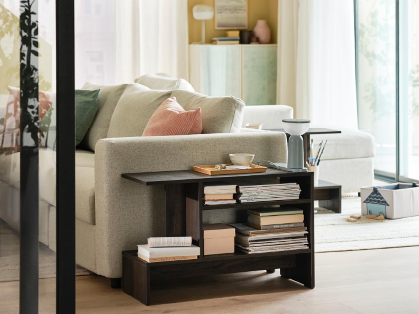 A HOLMERUD side table with many books on its shelves stands at the side of a VIMLE 3-seat sofa with extra cushions on it.