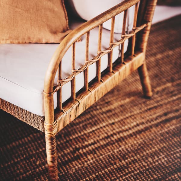 A HOLMSTA/FRÖKNABO armchair made from wood and rattan with cushions and a scatter cushion set on a LOHALS flatwoven rug.