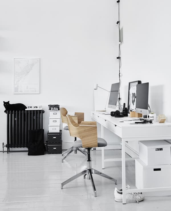 A home office workspace in the living room including two modern swivel chairs with wood backing and white work desks.