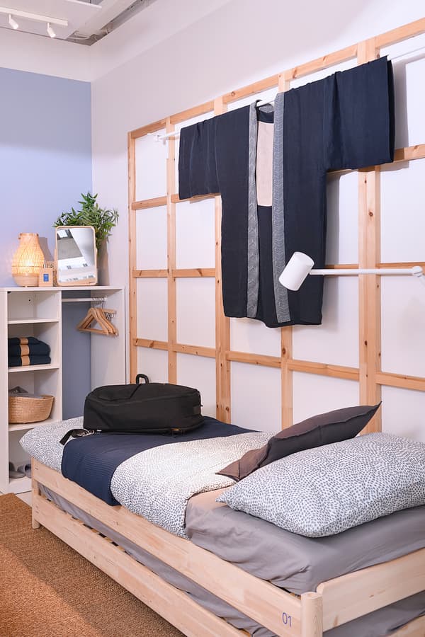 A hostel area featuring a single-sized bed, a cabinet and a wooden frame hung that is holding a towel.