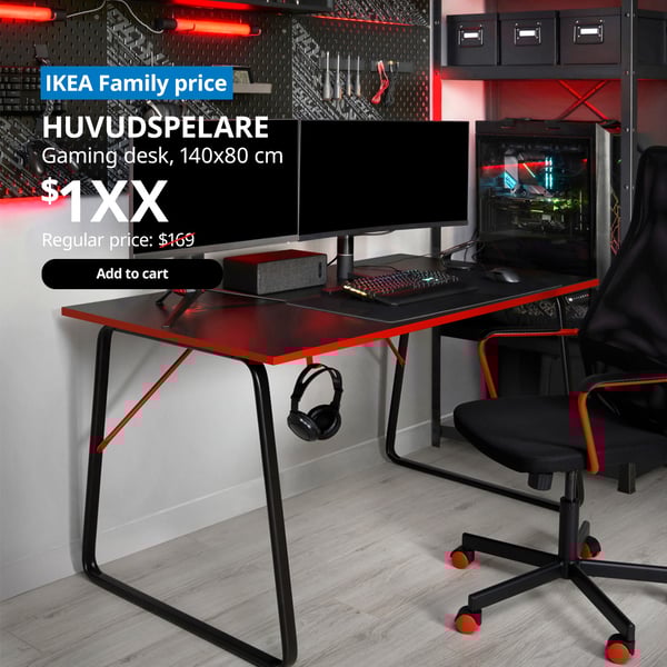 A HUVUDSPELARE gaming desk in a study/gaming room setting with a dual monitor screen. On the top left corner, a blue tag with white text that reads 