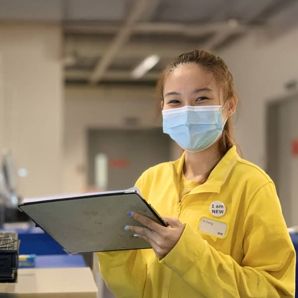 A IKEA staff wearing a mask while holding onto a tablet.